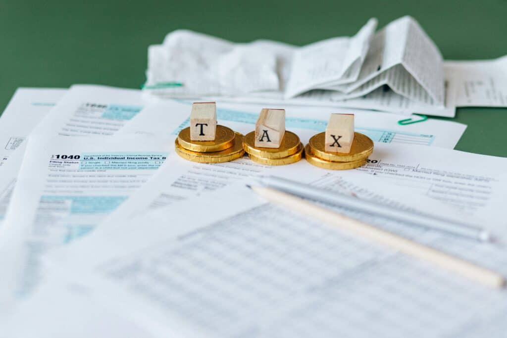 Three stacks of gold coins with wooden blocks spelling out tax on top of them.
