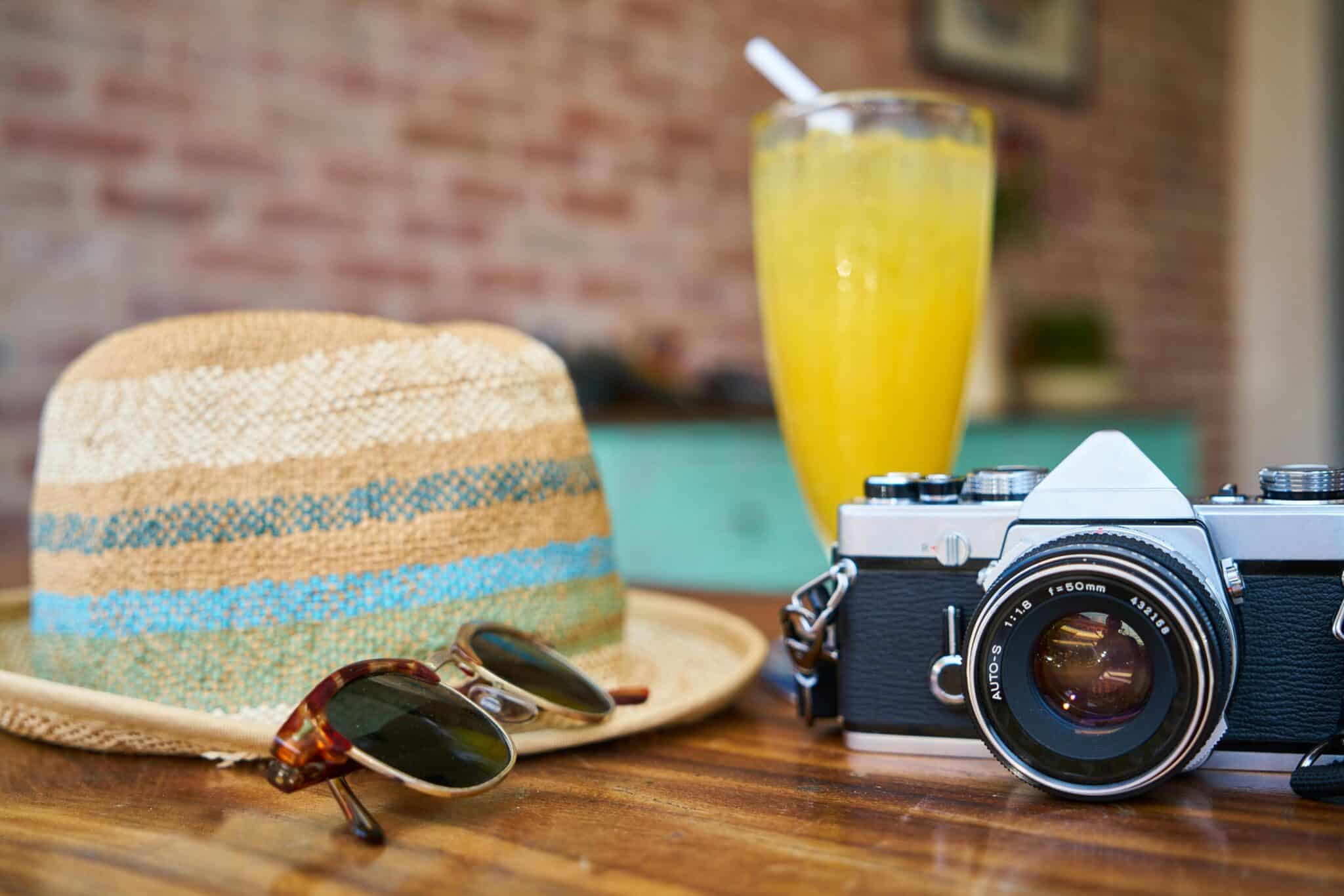 Close up of straw hat, sunglasses, camera, and fruity drink.